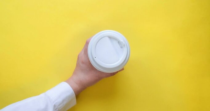 Craft paper coffee cup fills with drink and woman's hand take it. Coffee to go in a cup with a white lid on a yellow background. Looped 4K stop motion animation