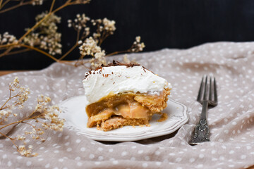Porción de tarta  con base de galletas con mantequilla, plátano, toffe y nata montada 