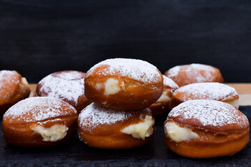 Bolas de masa dulce frita rellenas de crema con azúcar glas por encima, sobre plato de pizarra...