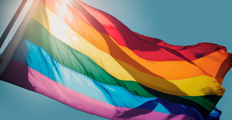 LGBT Flag waving in the bright sunny sky, as colorful symbol of strength and triumph of LGBTQ+ community in fight for pride, diversity, love, acceptance, inclusivity and equality. Generative AI.