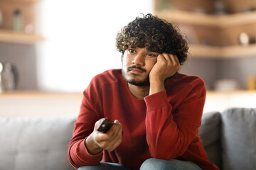 Boring Program. Portrait Of Upset Young Indian Man Watching TV At Home