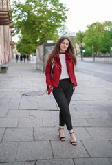 Beautiful Young Girl is Standing on the side Walk in Vilnius Old Town, Lithuania. Wearing Red jacket and Black Trousers. Beautiful Spring Day