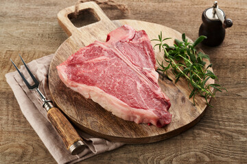 Thick Raw T-Bone Steak. Dry-aged Raw T-bone or porterhouse beef meat Steak with herbs and salt on dark background. Selective focus and copy space.