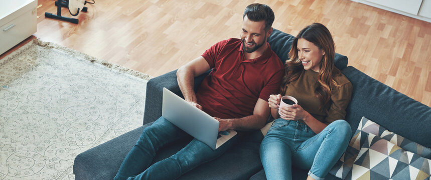 Happy young couple using laptop while sitting on the couch at home together