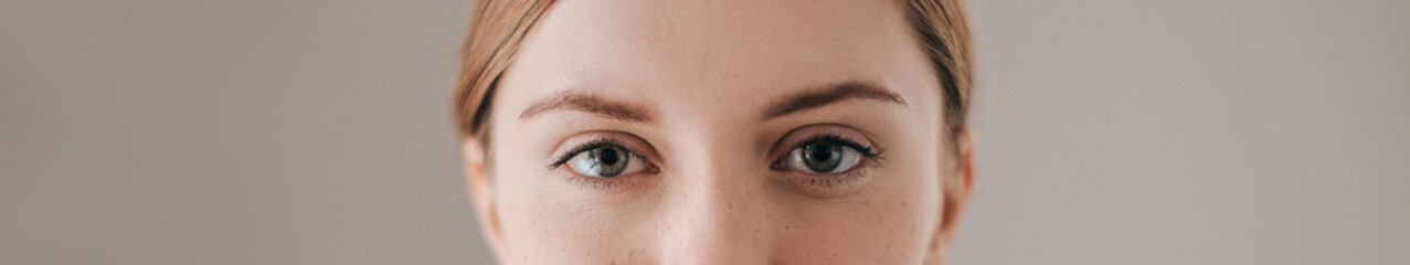 Close-up of beautiful freckled woman without make-up against grey background