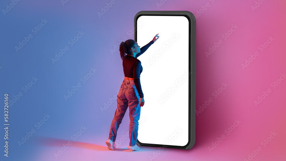 Poster full length shot of black lady touching screen of huge smartphone in neon light, mockup for app or w