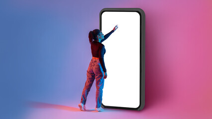 Full length shot of black lady touching screen of huge smartphone in neon light, mockup for app or...