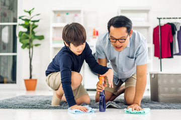 Father teaching asian kid little boy son use disinfectant spray bottle cleaning and washing floor wiping dust with rags while cleaning house together at home