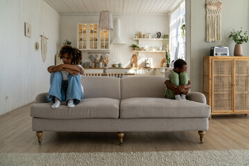 Upset unhappy African American family mother and son sitting separately on sofa, ignoring each...