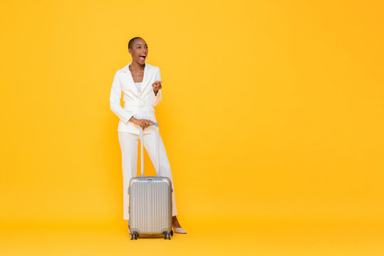 Stylish African American business woman traveler with suitcase being surprised and pointing to copy space in yellow color isolated backround  studio shot