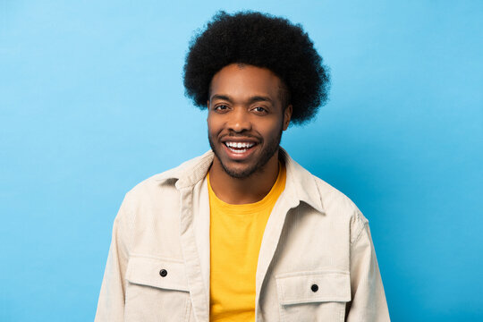 Happy positive Afro African American man smiling and looking at camera in light blue isolated background studio shot