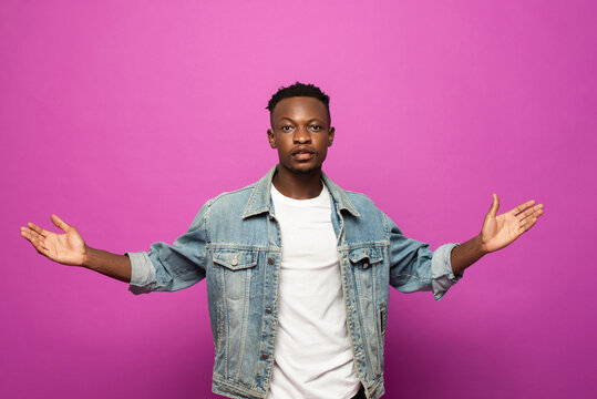 Young African man looking at camera with hand open gesture in purple color studio isolated background