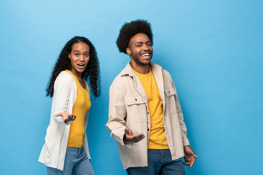Happy smiling Afro African American couple standing with open hand gesture in light blue studio isolated background