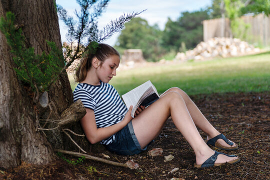 teen girl reading a book under a tree