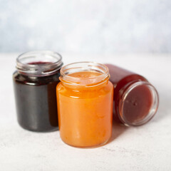 front view of set of small jam and vegetable jars in different colors without labels and shiny metallic lid covers isolated