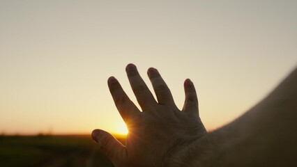 Mans hand reaches for sun, rays of sun break through his fingers. Hand of happy person reaches for sun. Sunset between fingers. Dream travelers hand, sun. Adventure, travel. Mans prayer in nature