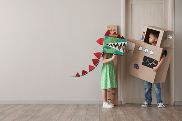 Little children in cardboard costumes playing near light wall