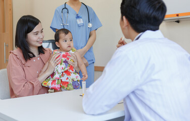 Mother holding cute baby in doctor's office Asian male pediatrician prescribes patient treatment. Medical