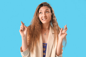 Beautiful young woman in jacket crossing fingers on blue background