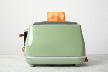 Modern toaster with crispy bread slice on white table