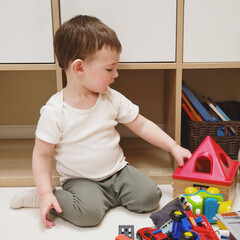 Toddler baby boy is playing with a sorter puzzle on a rug in the nursery. A small child is playing with toys. Kid aged one year eight months