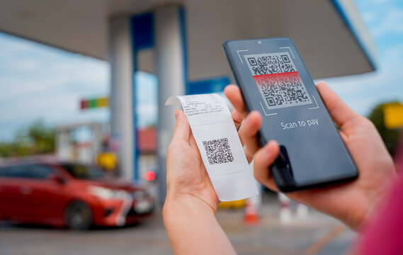 Woman using contactless payment by mobile phone with QR code at car filling station