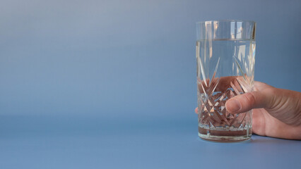 Woman's hand holding a glass of water on a blue background