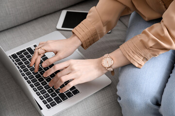 Obraz na płótnie Canvas Woman with wristwatch using laptop on sofa, closeup