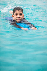 Fototapeta na wymiar Cute Little Asian Thai Boy, practicing swimming in the pool.