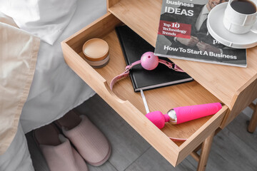 Open drawer with sex toys, notebook and cream in bedroom, closeup