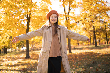 Happy young girl enjoying life and freedom during autumn season with closed eyes on the nature, breathing deeply in park with foliage in background.