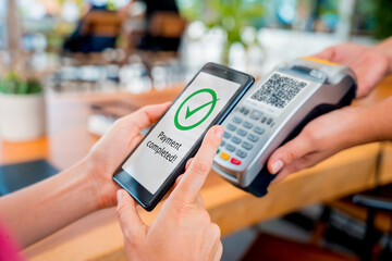Woman using contactless payment by mobile phone with QR code at cafe