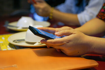 Customers are surfing the internet on their mobile phones while waiting for dinner to be ordered at the table. soft and selective focus.