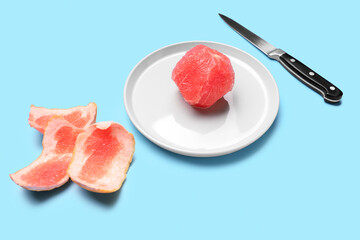 Plate with peeled grapefruit and knife on color background