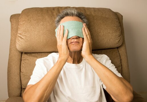 Older man sitting in an EZ chair with a warn compress over his eyes for pain relief