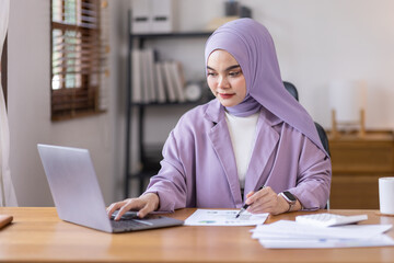 Portrait of Muslim Businesswoman Wearing Hijab Works on laptop computer at home, Does Document and Blueprints Analysis. Empowered Digital Entrepreneur Works on e-Commerce Startup Project