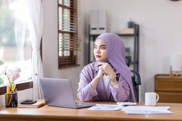Portrait of Muslim Businesswoman Wearing Hijab Works on laptop computer at home, Does Document and Blueprints Analysis. Empowered Digital Entrepreneur Works on e-Commerce Startup Project