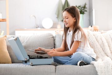 Little girl with record player sitting on sofa at home