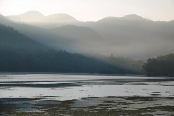 Landscape of a lake with mountain forest covered with light fog in the early morning