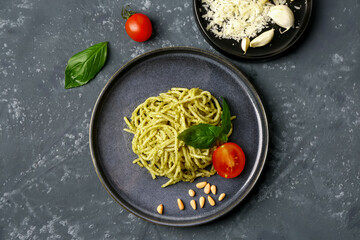 Plate with tasty pesto pasta and tomatoes on dark grunge background