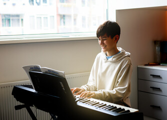 Teen boy enjoy playing practicing electronic piano keyboard in his free time in his room at home. Healthy living life style concept.