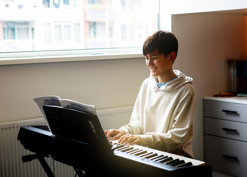 Teen Boy Enjoy Playing Practicing Electronic Piano Keyboard In His Free Time In His Room At Home. Healthy Living Life Style Concept.