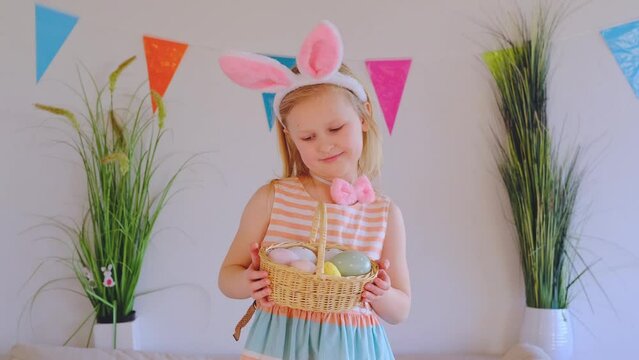 Happy little girl in rabbit ears holding Easter eggs in their hands at home.