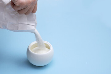 hand pours sugar into a sugar bowl on a blue background with copy space
