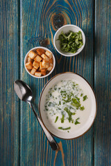 yogurt soup with herbs and crackers on a blue wooden table,top view