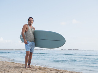 Hispanic surfer standing on the beach shore with a surfboard