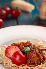 Tasty spaghetti with minced meat and cherry tomatoes on blue wooden background.
