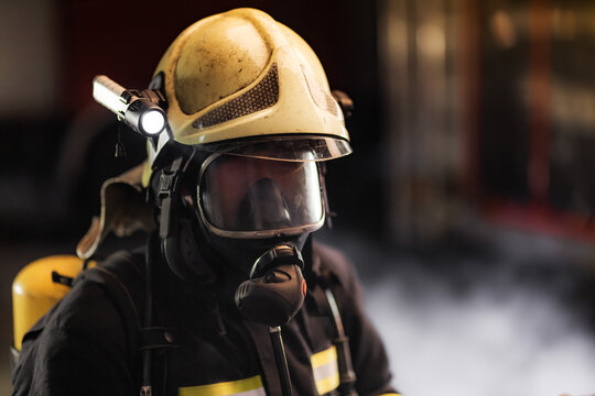 Fireman wearing full equipment.  Firefighter with protective helmet oxygen mask and flashlight. Smoke and fire trucks in the background.