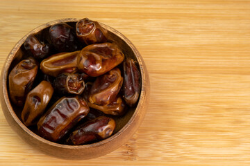 Dates fruits in wooden bowl on wooden background close up. Eating dried fruits. Vegan, vegetarian food
