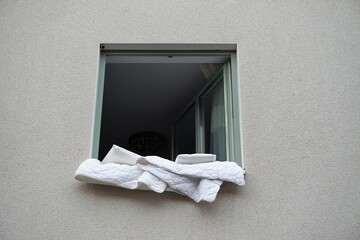 Weiße Hausfassade mit offenem Fenster und weißen Federkissen- und decken über Fensterbank zum...